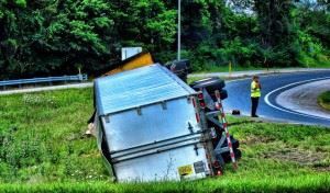 big rig truck rolled on its side in a field near a road